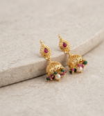traditional gold-plated jhumka earrings featuring ruby-red stone studs and dangling pearl and multi-colored bead accents.