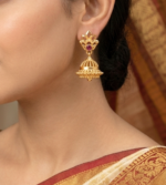 gold-plated jhumka earrings featuring a decorative floral stud accented with a red ruby-like stone and a textured bell-shaped drop. - Image 2