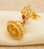gold-plated jhumka earrings featuring a decorative floral stud accented with a red ruby-like stone and a textured bell-shaped drop. - Image 3